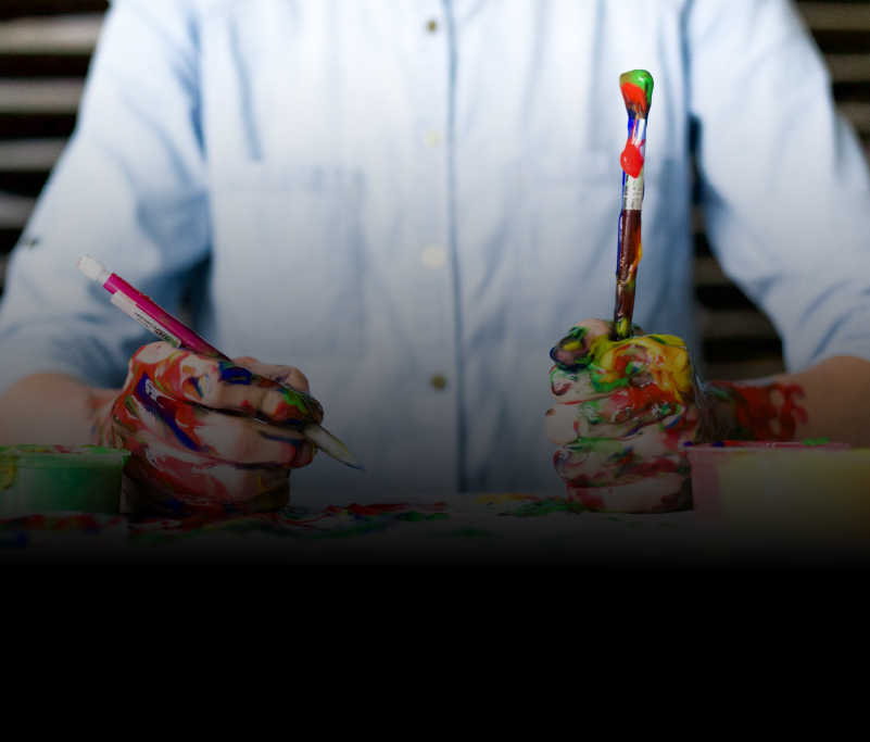 Person holding paint brush and pencil covered in paint 