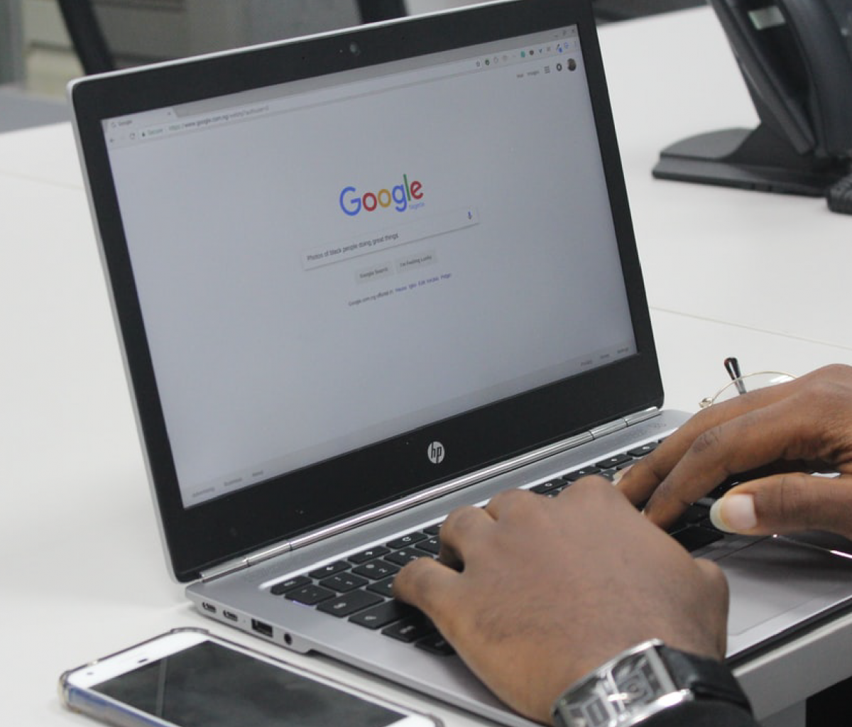 Laptop on desk with persons hands typing on keyboard and "Google" on the screen