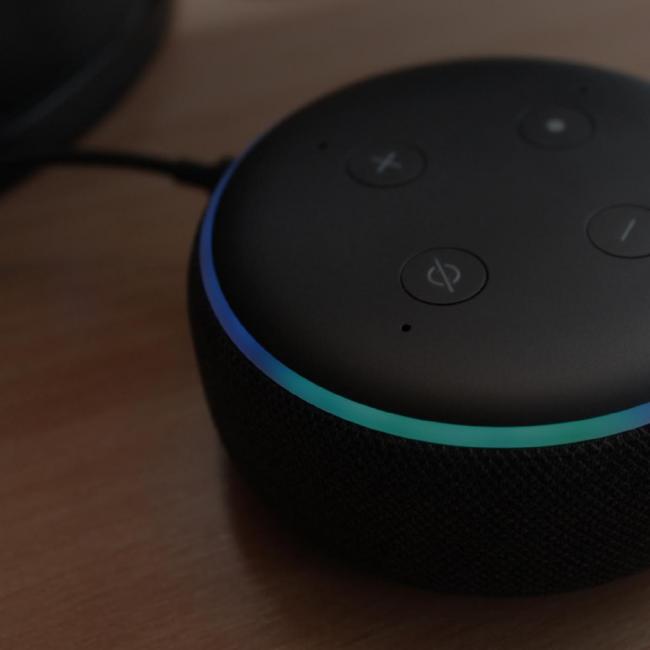 Image of an Amazon Alexa device sitting on a table with a dark overlay 