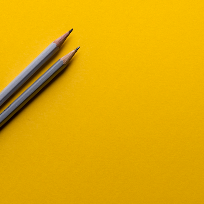 Two gray pencils for writing alt text for a website sitting on a yellow background 