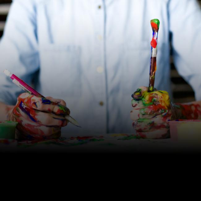 Person holding paint brush and pencil covered in paint 